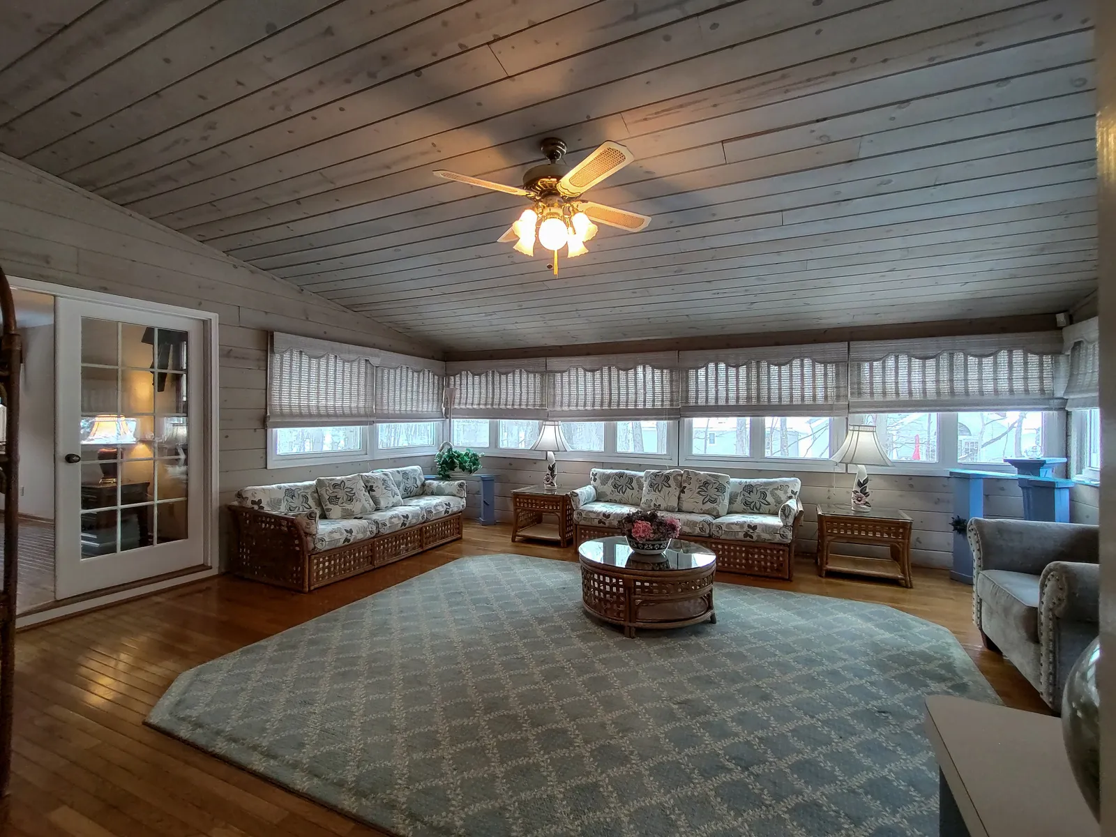 Sun-filled four-season sunroom with a whitewashed shiplap ceiling, a wraparound band of windows, and wicker seating — a Fully Focused Media interior