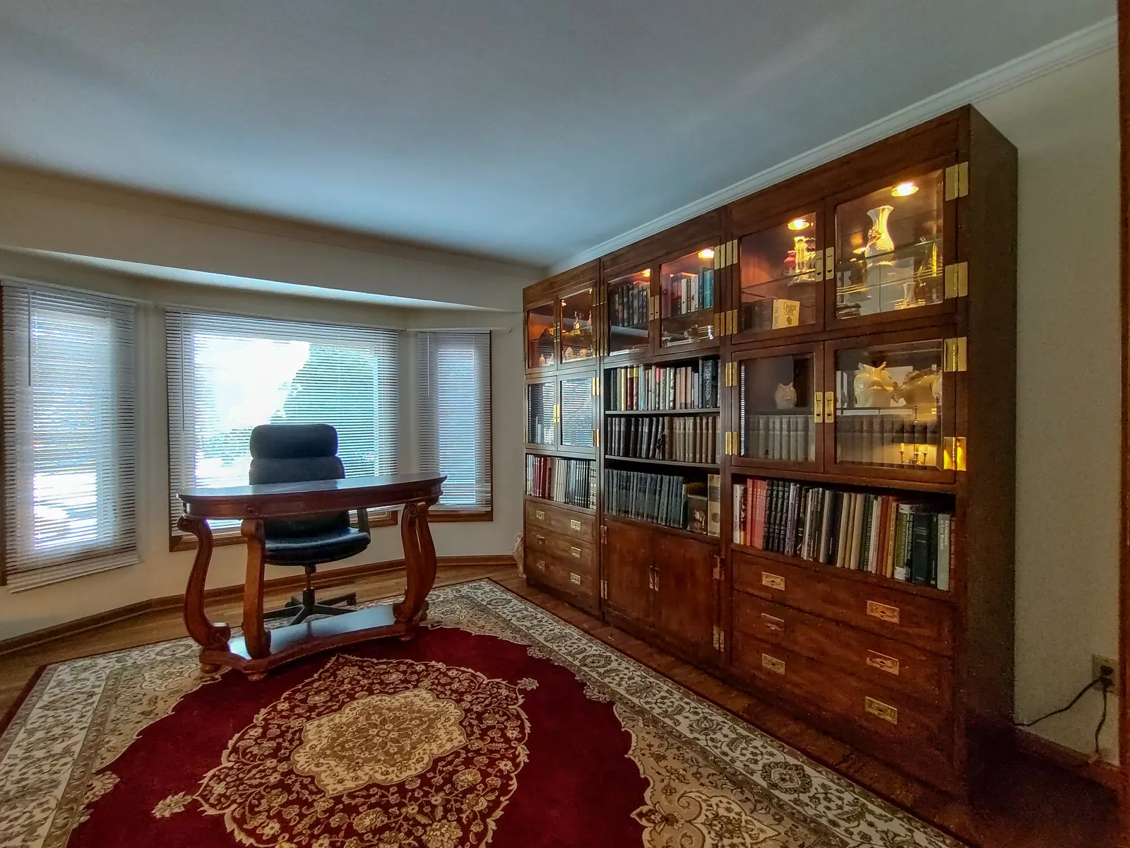 Home office and library with a wood desk, executive chair, and a floor-to-ceiling lighted bookcase styled for a lifestyle feature