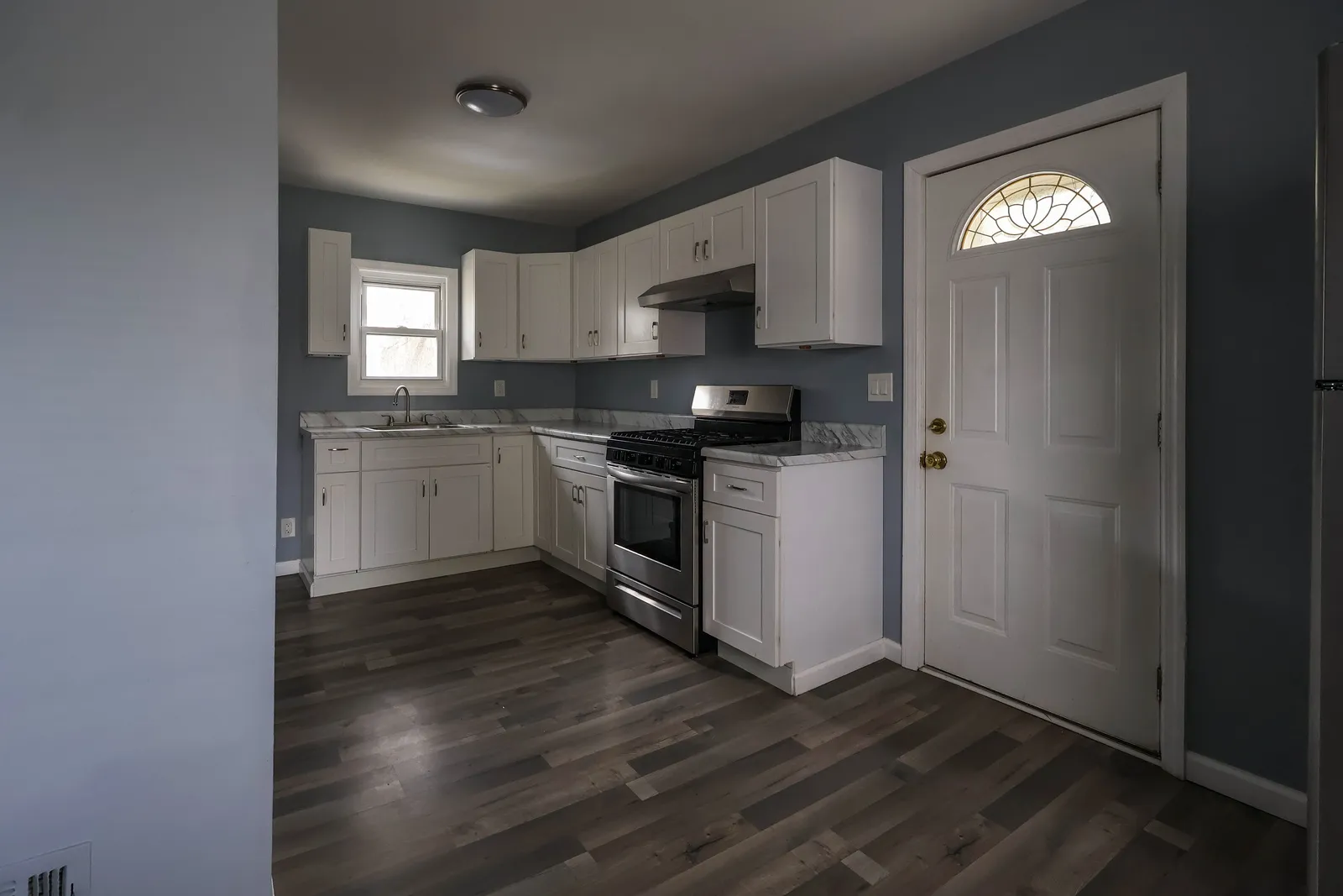 Renovated kitchen with white shaker cabinets, marble-look countertops, and stainless steel appliances over dark hardwood floors
