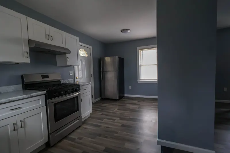 Modern white-shaker kitchen with a stainless gas range, marble countertops, and dark hardwood floors