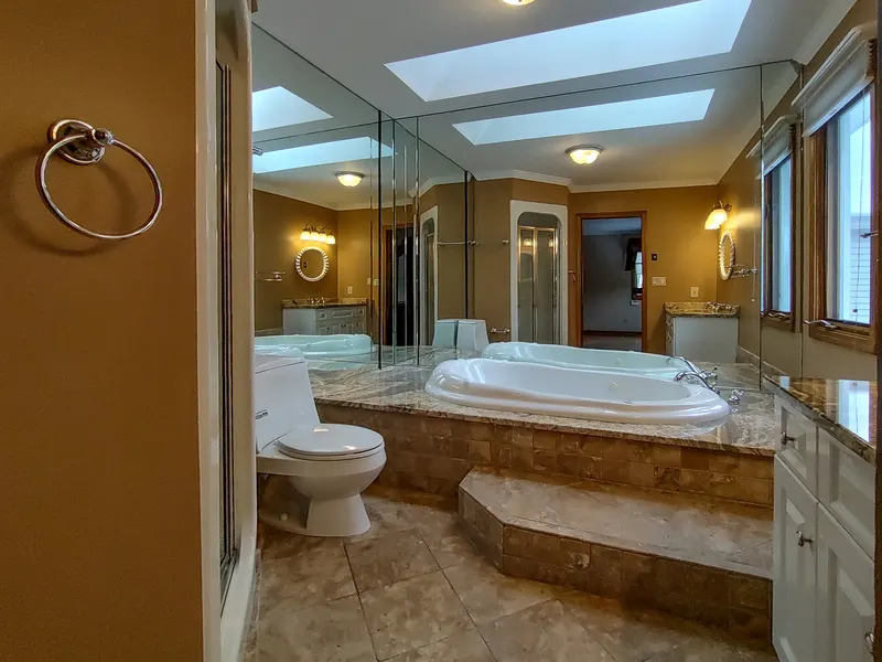 Primary bathroom with a raised marble-surround soaking tub, a glass shower enclosure, and skylights
