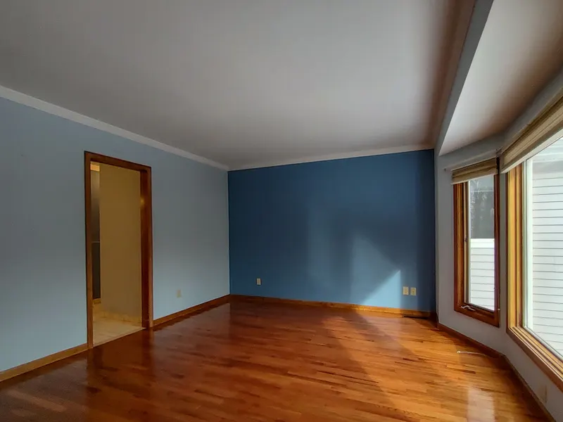 Bright primary bedroom with a deep blue accent wall, polished hardwood floors, and a large window