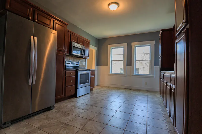 Kitchen with cherry wood cabinetry, a stainless French-door refrigerator and range, tile backsplash, and wainscoting