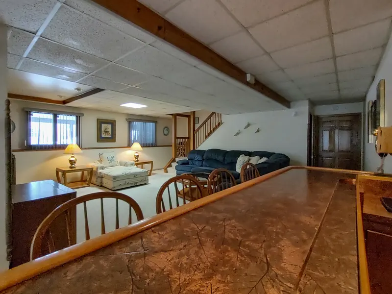 Finished basement rec room with a sectional sofa, a brick fireplace, and a beamed drop ceiling