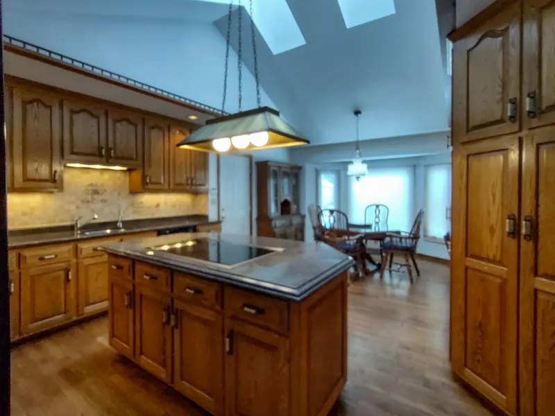Open-plan vaulted kitchen with a dark granite island cooktop, oak cabinetry, and a skylight overhead
