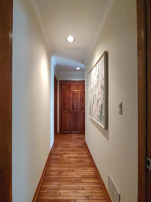 Residential hallway with hardwood floors, recessed lighting, and framed artwork leading to paneled double doors